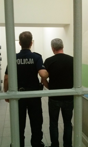 zatrzymany stoi za kratą razem z policjantem