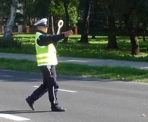 Policjant ruchu drogowego trzyma lizaka w ręce i zatrzymuje auta do kontroli