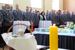 Kadra kierownicza wielkopolskiej Policji, przed nimi stół wielkanocny, a na pierwszym planie koszyk wielkanocny i zapalona świeca.