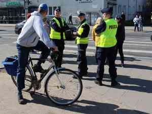 policjanci stojąc przy pasach rozmawiają z rowerzysta