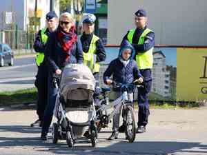3 policjantow stoi przy pasach wraz z kobieta ktora pcha wózek z dzieckiem