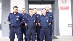 Sześciu umundurowanych policjantów stoi na tle budynku Komendy Powiatowej Policji w Jarocinie