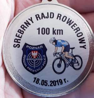 Pamiątkowy medal na którym widnieje cyfra 100, symbol oddziału prewencji Policji i data rajdu oraz grafika rowerzysty.