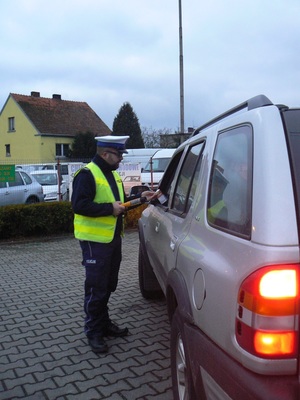 policjant zatrzymał do kontroli kierowcę, bada jego stan trzeźwości i wręcza darmowy alkotest pouczając o tym co grozi za jazdę pod wpływem alkoholu