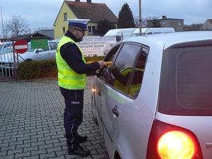 policjant zatrzymał do kontroli kierowcę, bada jego stan trzeźwości i wręcza darmowy alkotest pouczając o tym co grozi za jazdę pod wpływem alkoholu