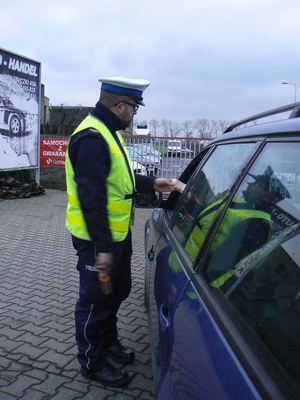 policjant zatrzymał do kontroli kierowcę, bada jego stan trzeźwości i wręcza darmowy alkotest pouczając o tym co grozi za jazdę pod wpływem alkoholu