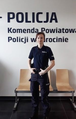 Umundurowana policjantka stoi na tle loga Komendy Powiatowej Policji w Jarocinie