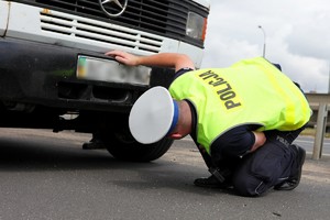 Policjant ruchu drogowego sprawdza podwozie zatrzymanego samochodu.