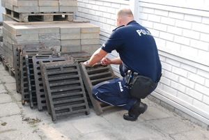 policjant stoi przy zabezpieczonych studzienkach kanalizacyjnych