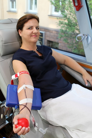 kobieta siedząca na fotelu do pobierania krwi, rękę ma wyciągniętą, a do niej podłączoną aparaturę d pobierania krwi