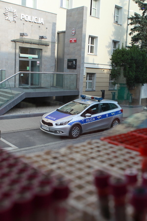 zdjęcie z wnętrza krwiobusu, na pierwszym planie probówki z krwią, na drugim radiowóz zaparkowany przed budynkiem komendy