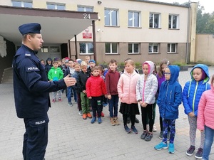 Policjant w mundurze rozmawia z dziećmi na ulicy o bezpieczeństwie na drodze