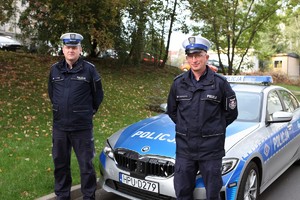 mł. asp. Daniel Szustakowski oraz asp. sztab. Ireneusz Turek pozują do zdjęcia w mundurach na tle oznakowanego BMW