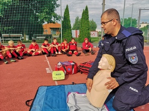 Ratownik medyczny w policyjnym mundurze uczy pierwszej pomocy uczestników sportowej kolinii