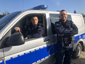Dwóch policjantów - jeden za kierownicą radiowozu, drugi stoi obok