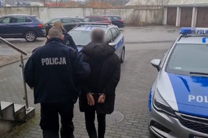 Umundurowany policjant prowadzi zatrzymanego mężczyznę