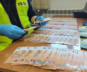 policjant z zabezpieczonymi fałszywymi banknotami