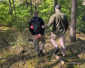 policjant zakuwa zatrzymanego, który leży na trawie w kajdanki; policjant z zatrzymanym idą przez las