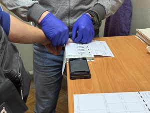 policjantka z zatrzymanym; policjant ściąga odciski palców zatrzymanego