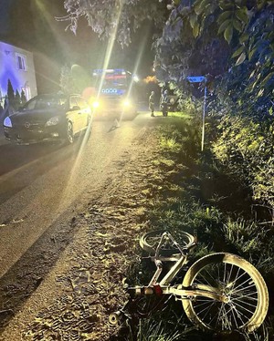 Rower leżący na poboczu drogi, w tle światło z reflektorów samochodowych