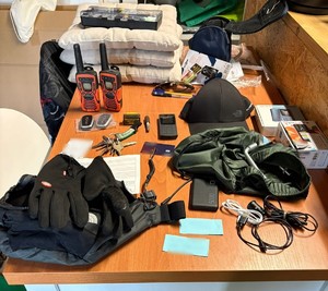 policjanci prowadzą zatrzymanych; zabezpieczone przedmioty; odzyskane auta