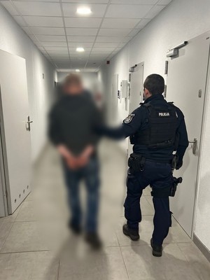 policjant prowadzi zatrzymanego przez korytarz na komendzie