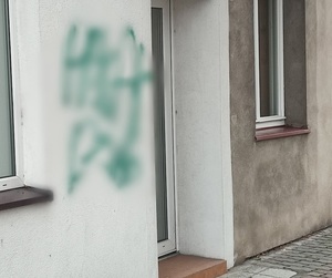 policjanci z zatrzymanym; pomalowane sprayem ściany budynków