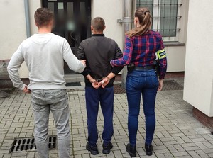 policjanci z zatrzymanym; pomalowane sprayem ściany budynków