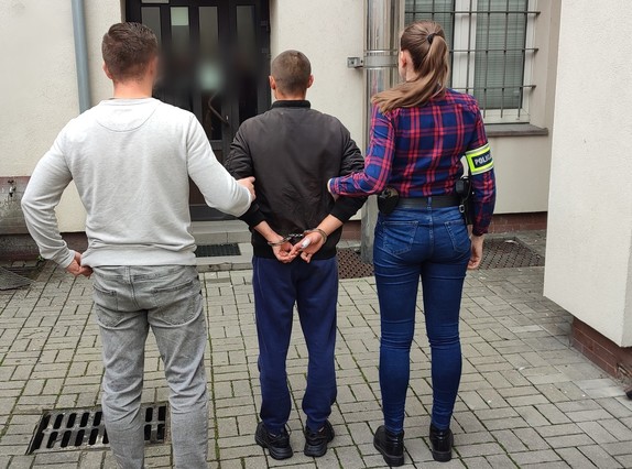 policjanci z zatrzymanym; pomalowane sprayem ściany budynków