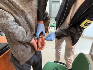 policjant zakuwa w kajdanki z tyłu ręce zatrzymanego