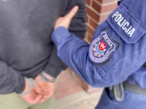 mężczyzna z rękoma zakutymi z tyłu kajdankami, policjant trzyma go za ramię