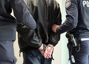 policjanci trzymają mężczyznę z rękoma zakutymi w kajdanki na plecach