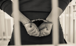 mężczyzna z rękoma skutymi kajdankami za kratami