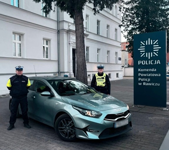 policjanci przed komendą stoją przy nieoznakowanym radiowozie