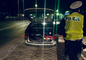 policjant z ruchu drogowego, przed nim samochód z otwartym bagażnikiem