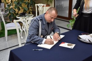 zdjęcie kolorowe, zastępca komendanta wojewódzkiego podczas wpisu do księgi pamiątkowej